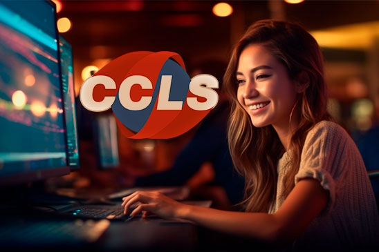 CCLS Class. Image description: Young woman smiling while using a computer in a room with CCLS logo on background.
